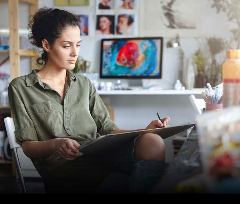 Female artist sketching with pencil in art studio, focused on creating detailed artwork.