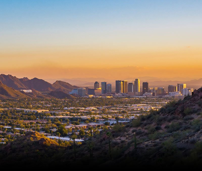 A beautiful view of the Scottsdale, Arizona skyline at sunset, featuring modern downtown architecture and desert landscapes under a colorful desert sky.