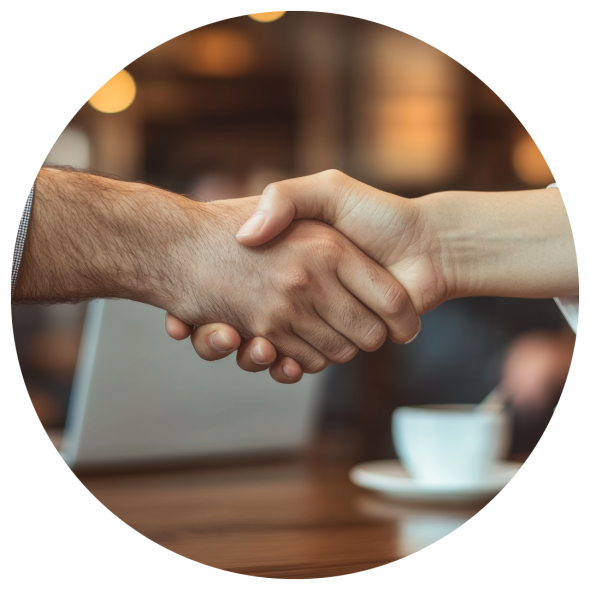 A handshake in a coffee shop, with a laptop and a coffee cup in the background.