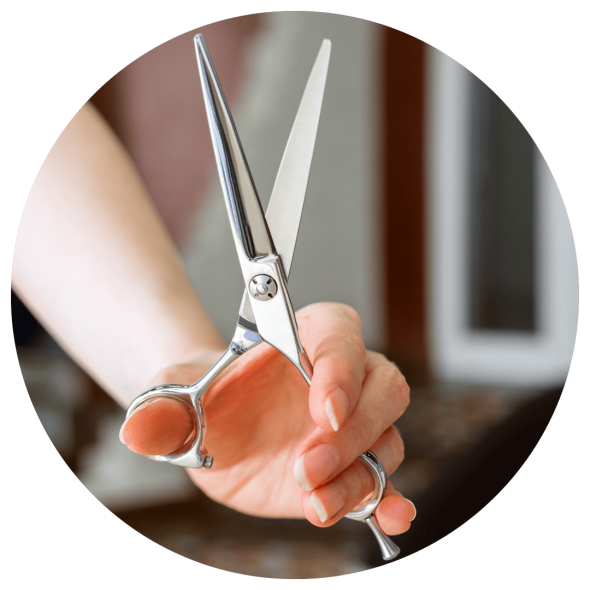 A close up image of hair dresser's hand holding a pair of shears in a salon.
